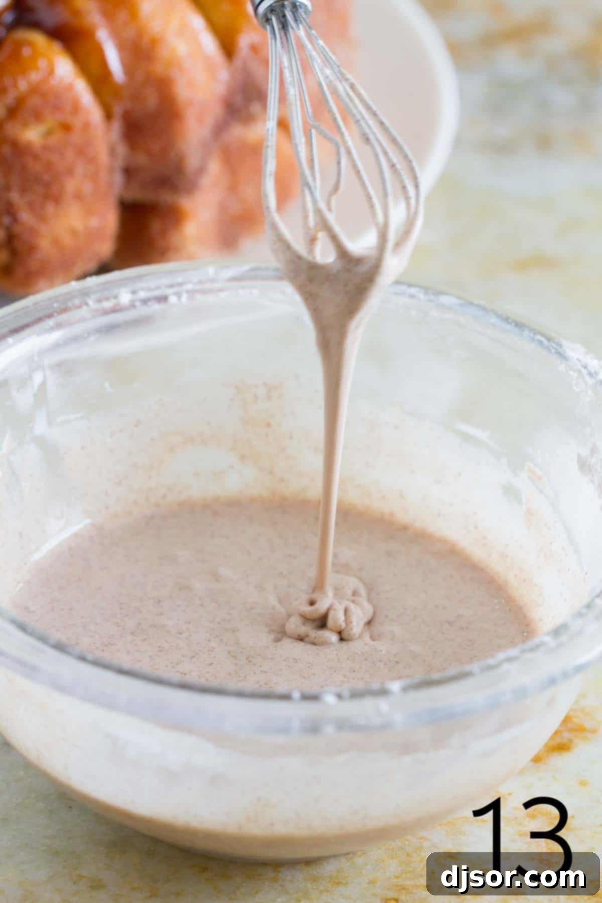 Cinnamon Glaze Preparation Close-up of a whisk dripping with rich, white cinnamon glaze, ready to be poured over Monkey Bread