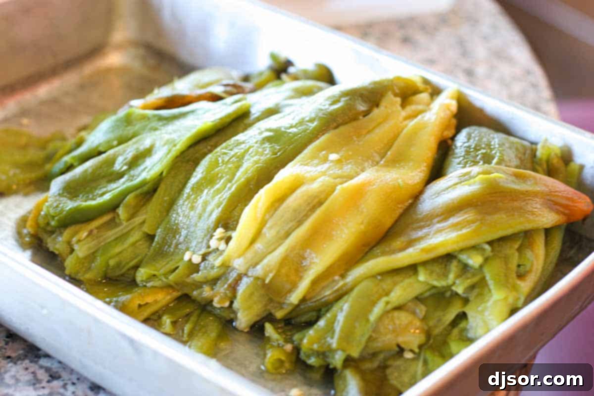 Homemade Chile Rellenos: Roasted Chiles A wide, shallow dish brimming with freshly roasted green chiles, their skins slightly charred and glistening, ready for peeling and preparation.