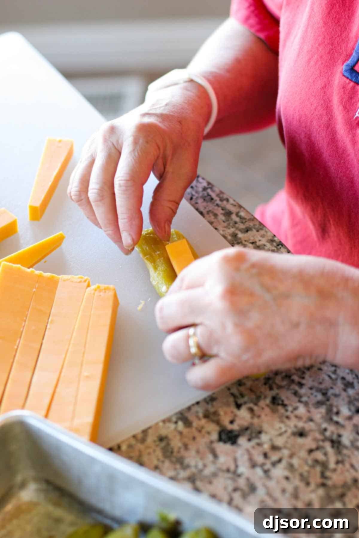 Homemade Chile Rellenos: Stuffing Cheese A skilled hand carefully stuffing a long piece of golden cheddar cheese into a vibrant green chile, preparing it for its crispy batter coating.