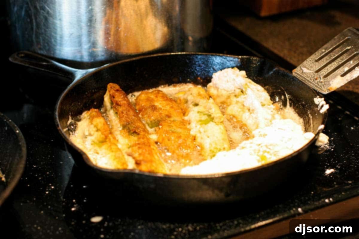 Homemade Chile Rellenos: Frying to Perfection A cast iron skillet sizzling with hot oil, as several batter-dipped, cheese-stuffed chile rellenos fry to a perfect golden crisp.