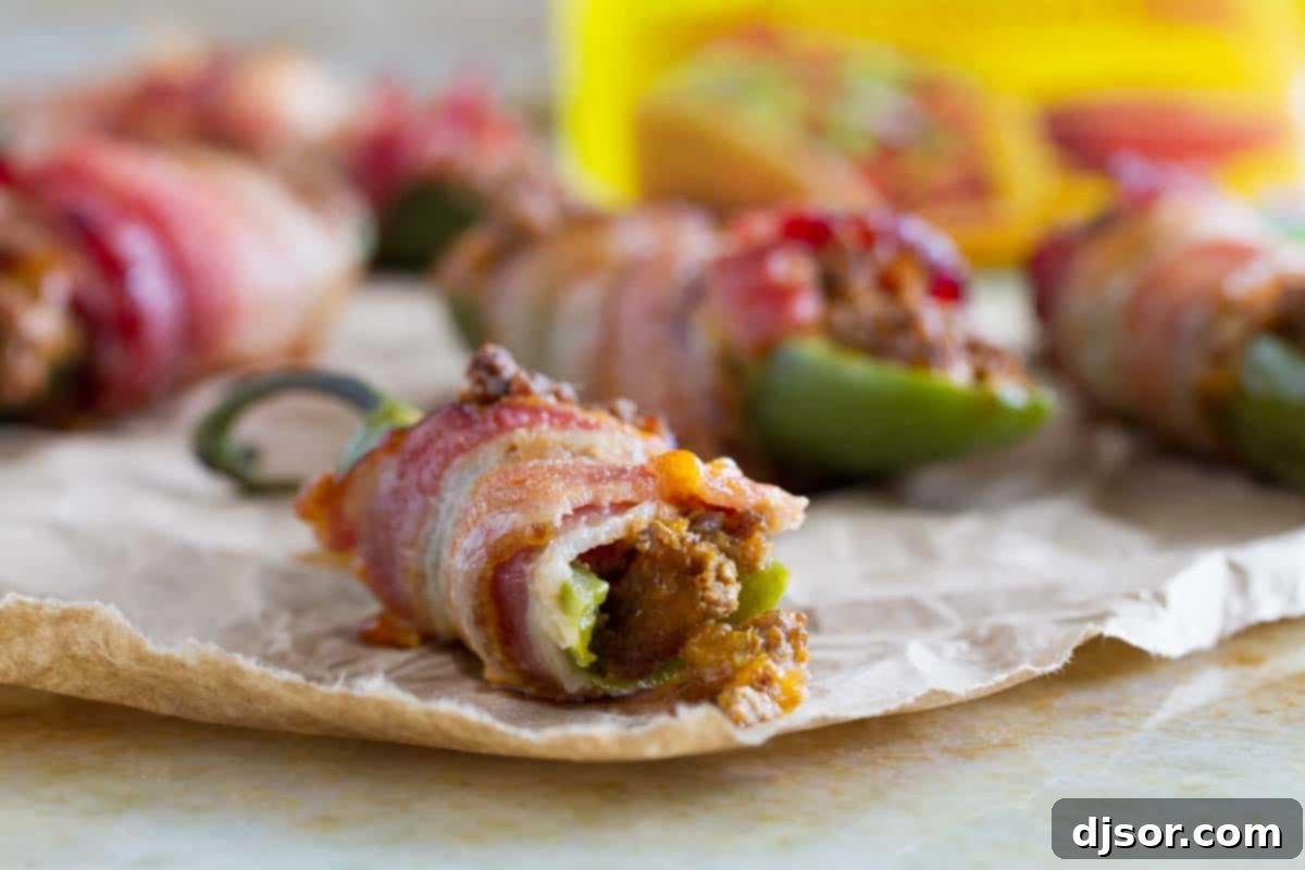 What is better than cheese stuffed jalapeño poppers? Bacon wrapped jalapeños that are stuffed with taco filling! These Bacon Wrapped Jalapeño Poppers with Taco Filling take a normal jalapeño popper and give them a delicious Tex-Mex twist. close up of bacon wrapped jalapeno popper with bite taken