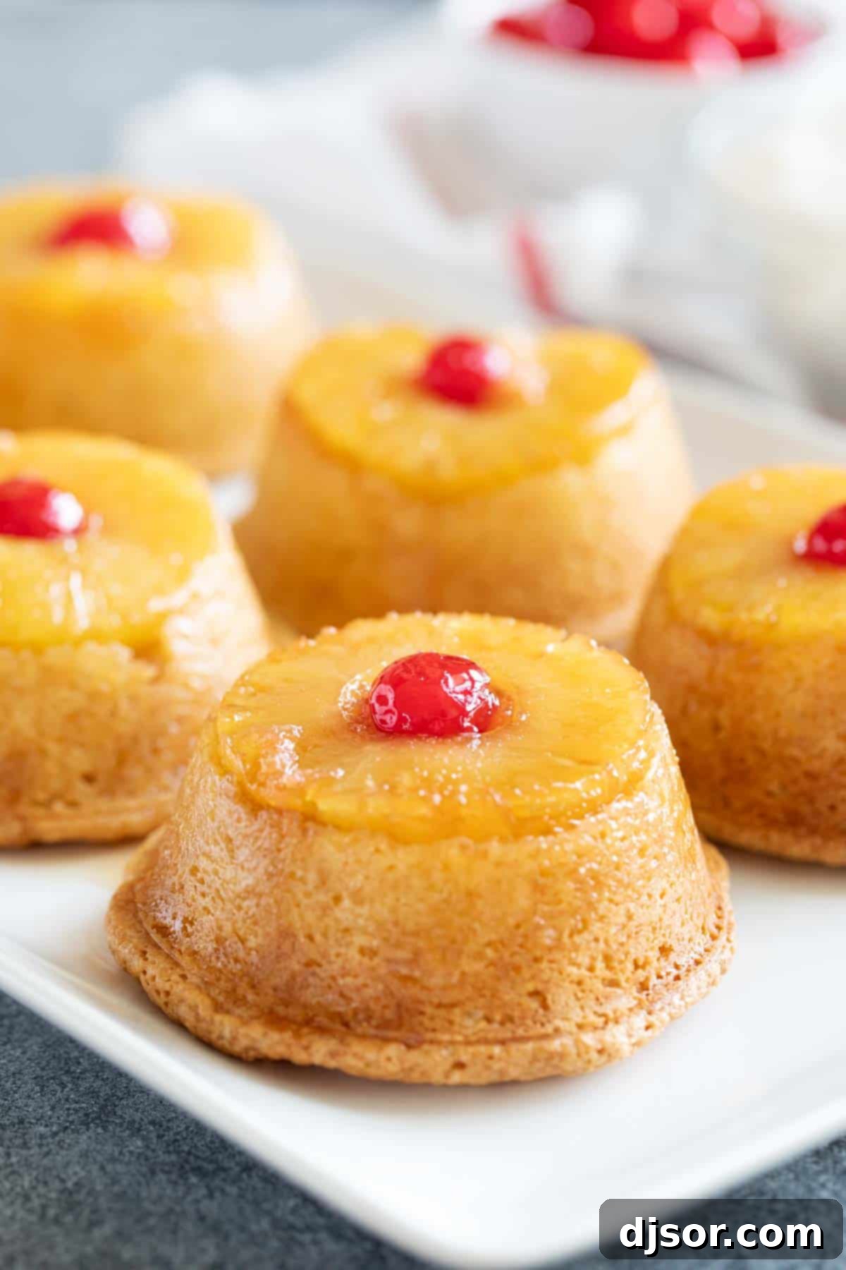 Pineapple upside down cupcakes arranged on a tray, showing the inviting pineapple and cherry topping. A tray filled with freshly inverted Pineapple Upside Down Cupcakes, each topped with a glossy pineapple ring and a single maraschino cherry.