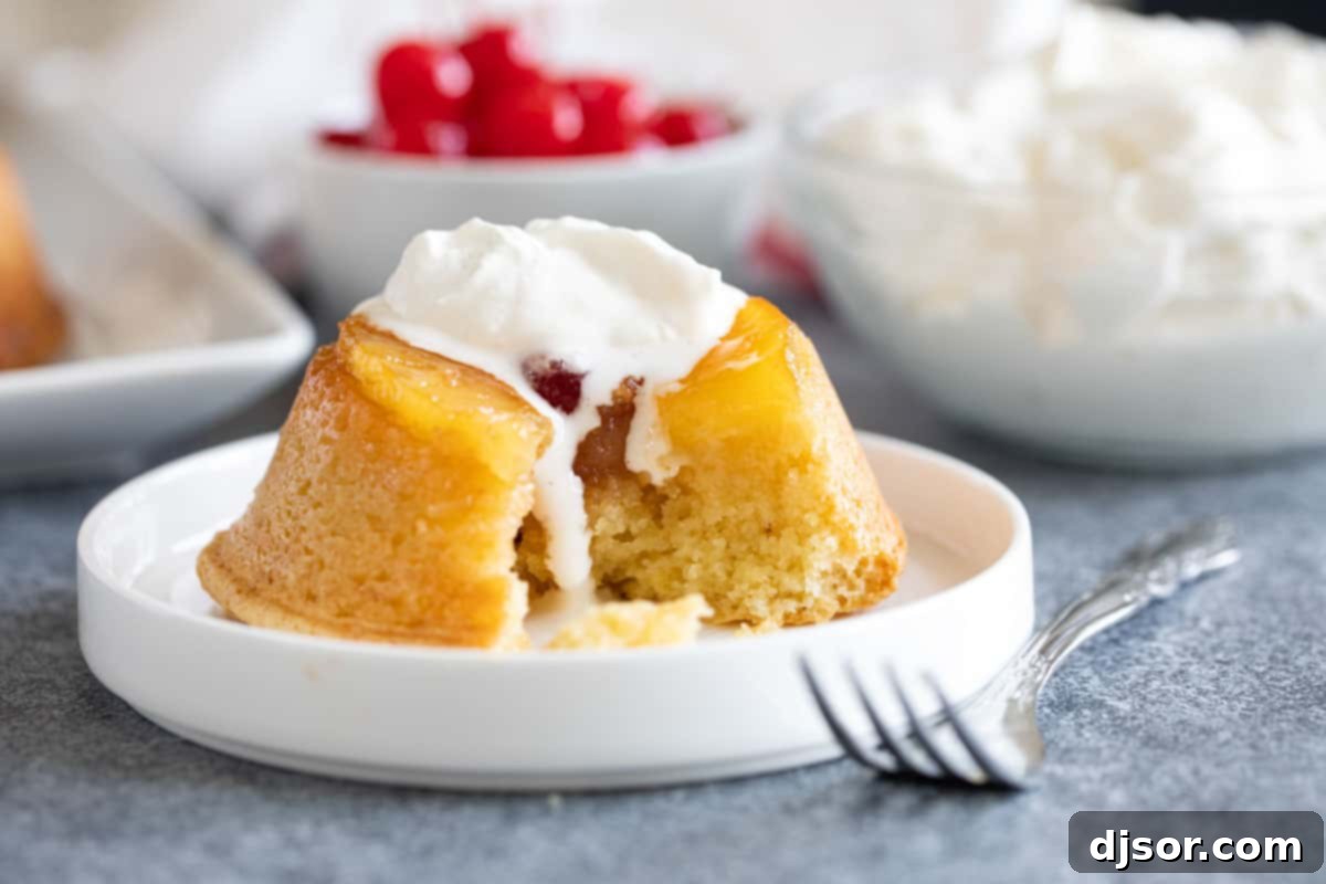 Pineapple upside down cupcake with whipped cream, showing a bite taken, highlighting the moist cake. A close-up shot of a Pineapple Upside Down Cupcake, topped with a swirl of fresh whipped cream, with a small bite taken to reveal the tender cake inside.
