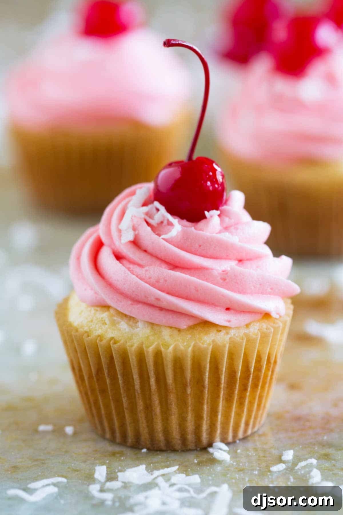 A single perfectly frosted coconut cherry cupcake, topped with a bright red maraschino cherry.