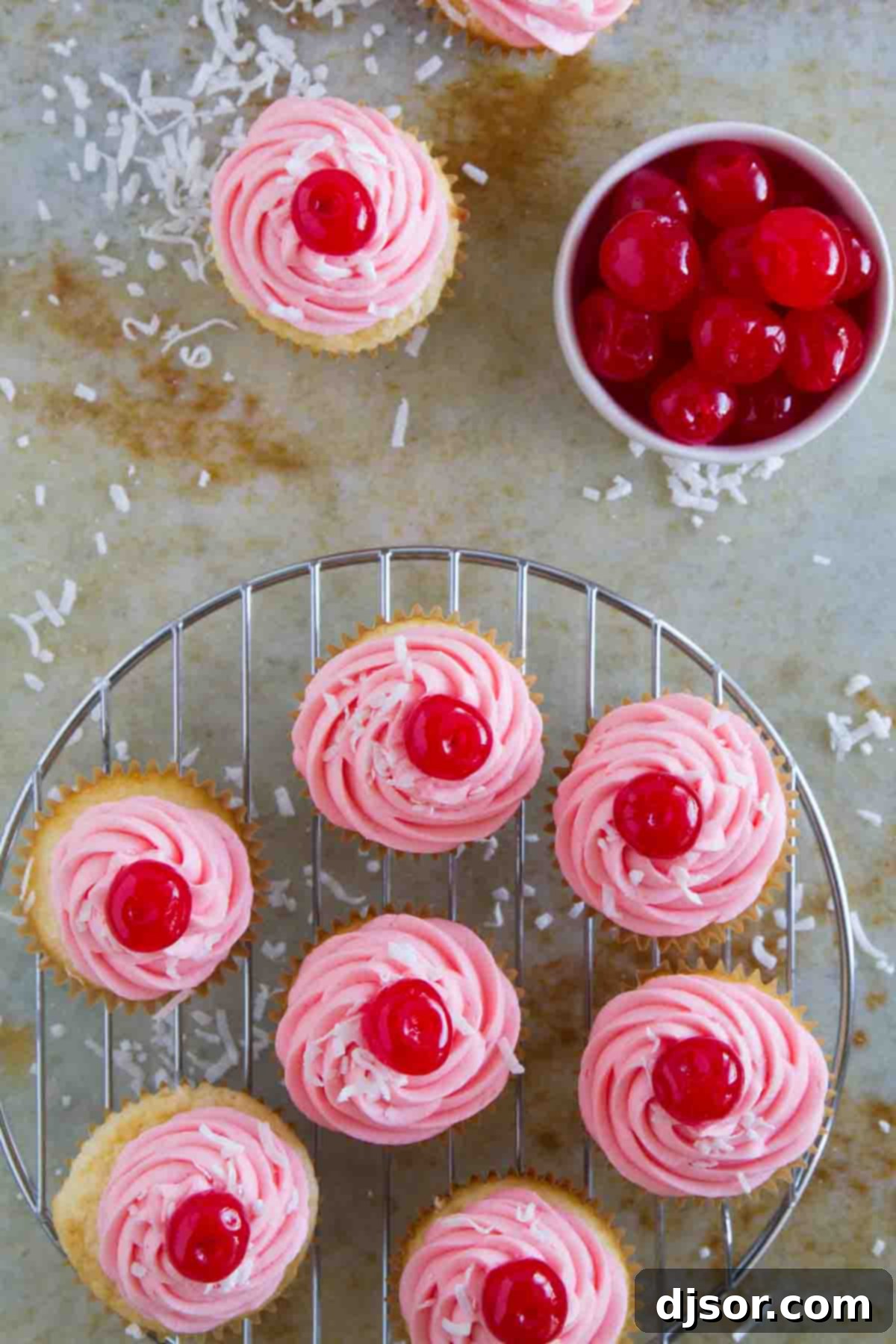 A batch of bright pink frosted cupcakes, each adorned with a maraschino cherry, displayed beautifully.
