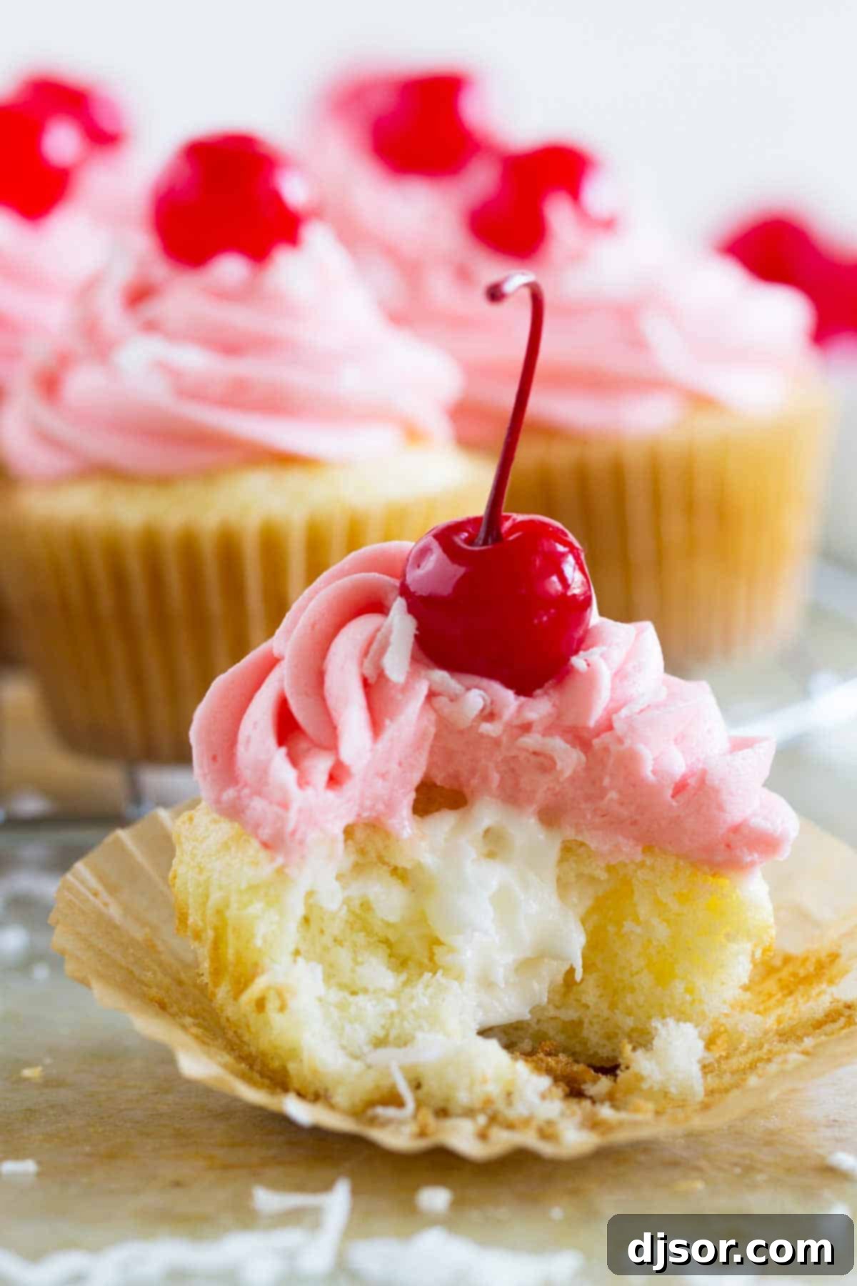 Close-up of a filled coconut cupcake, showing the creamy coconut center and pink cherry buttercream.