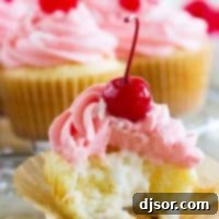 A beautifully frosted coconut cherry cupcake with creamy filling visible.