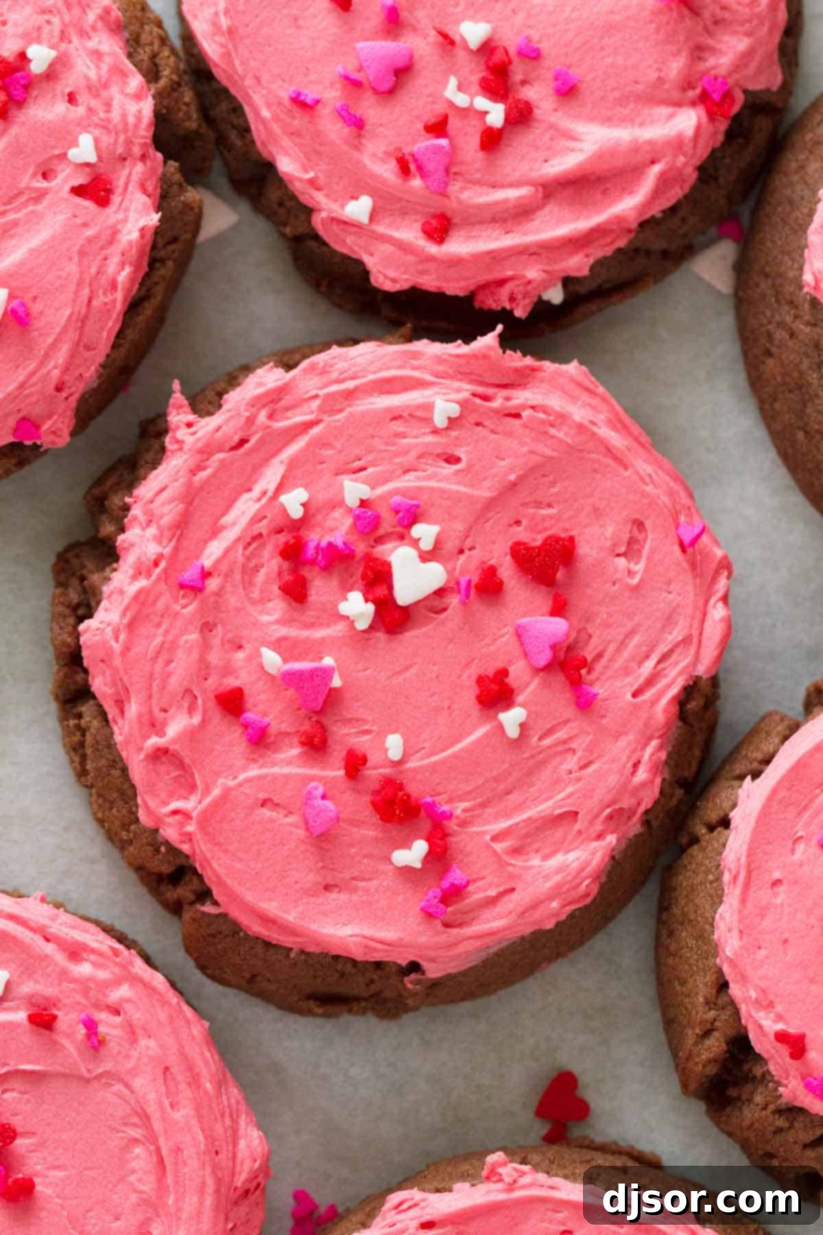Close-up overhead view of a freshly baked chocolate sugar cookie adorned with vibrant pink buttercream frosting and colorful sprinkles, perfect for a festive treat.