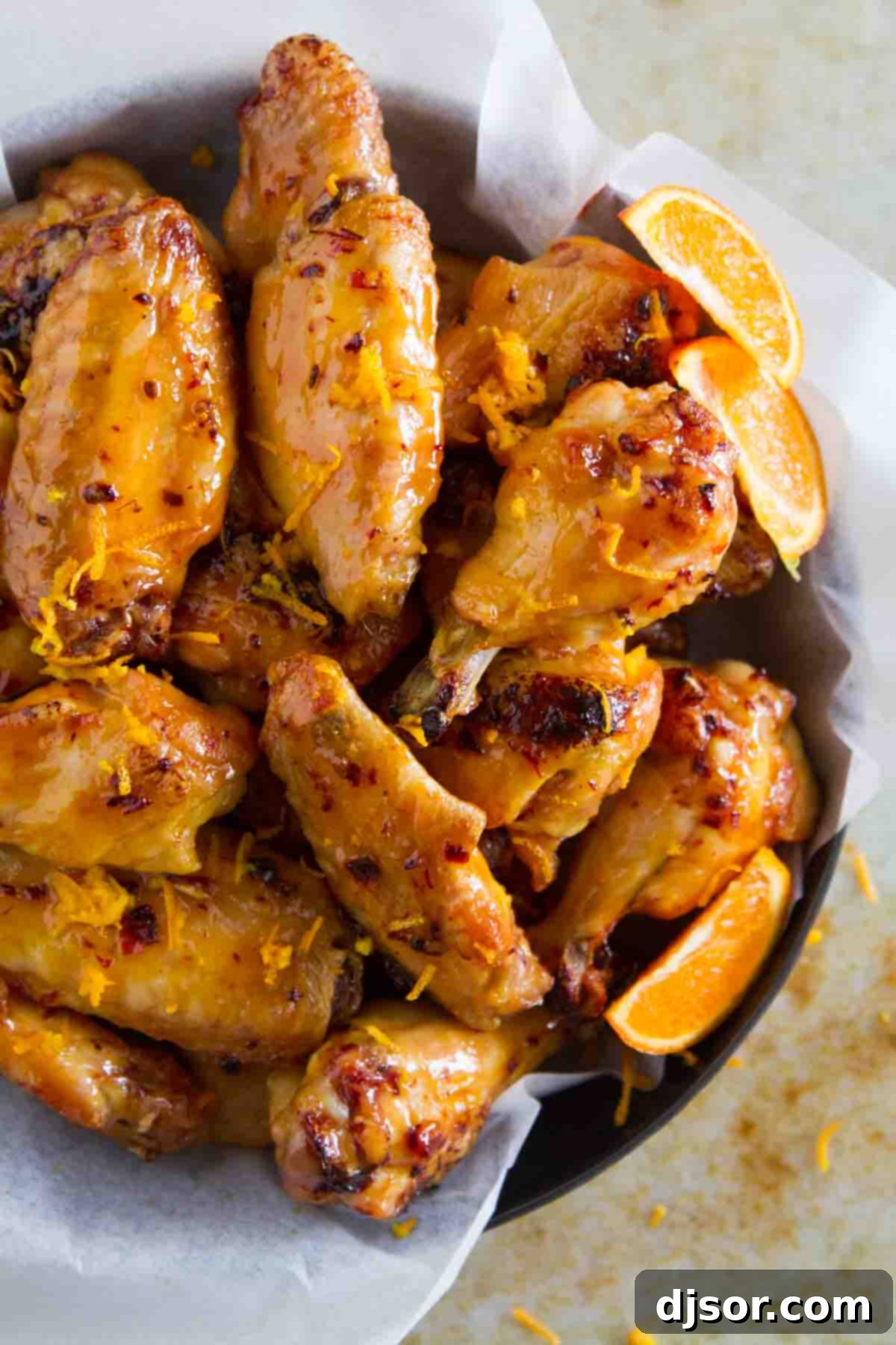 A bowl overflowing with perfectly glazed Chipotle Orange Chicken Wings, garnished with fresh orange zest.