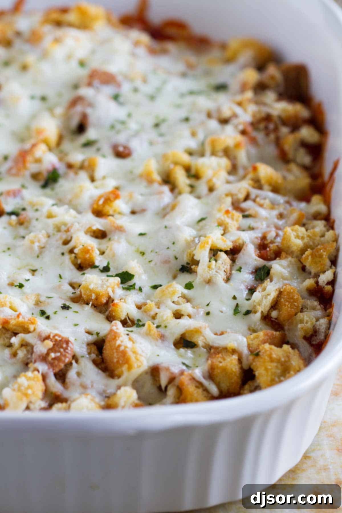 Close-up of bubbling, melted cheese topping a Chicken Parmesan Casserole in a white baking dish.