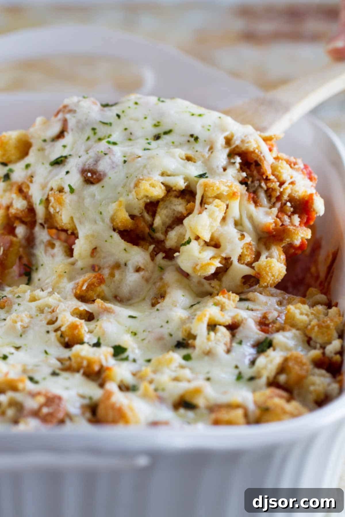 A serving spoon lifting a portion of cheesy Chicken Parmesan Casserole from the baking dish.