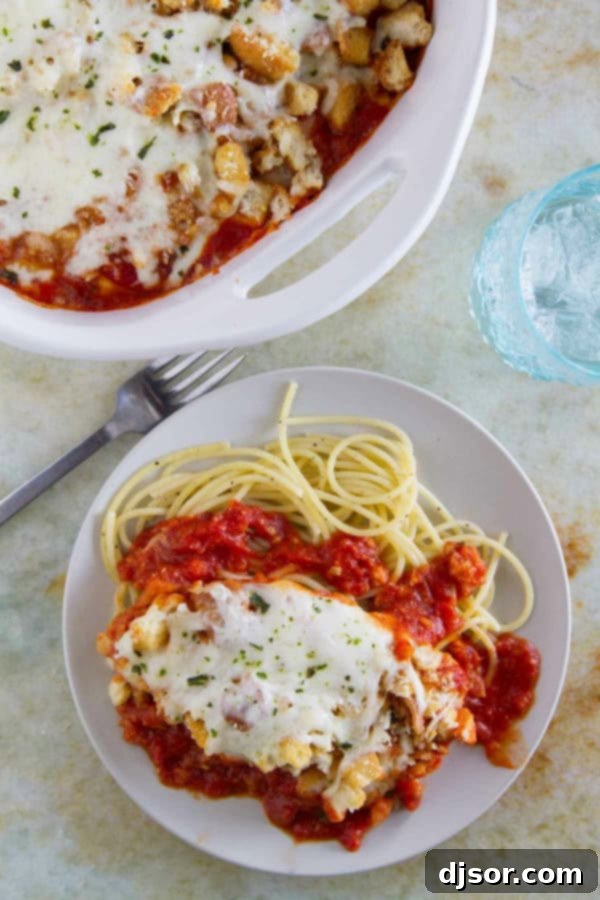 A generous serving of Chicken Parmesan Casserole presented over a bed of al dente spaghetti noodles, ready to eat.