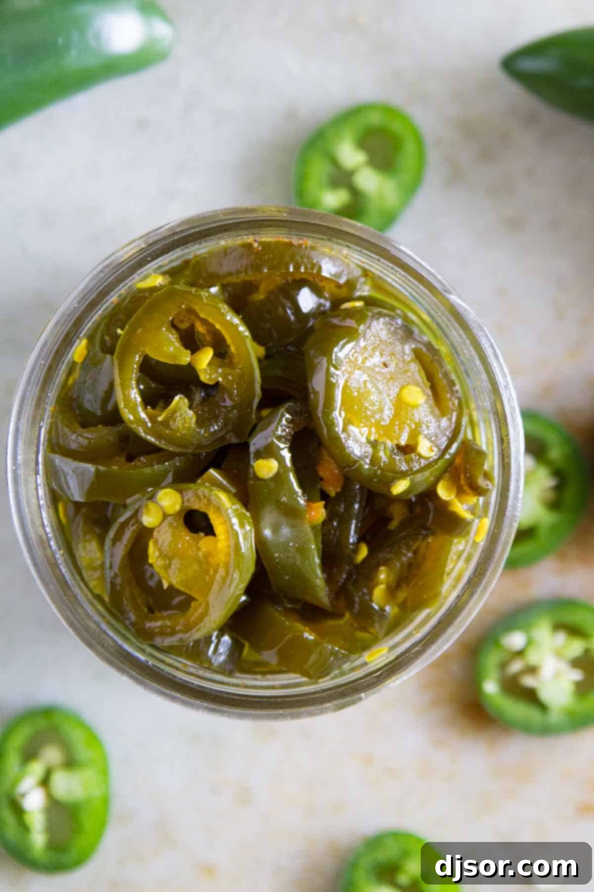 A top-down view of a glass jar filled with vibrant green candied jalapeños, ready for storage.