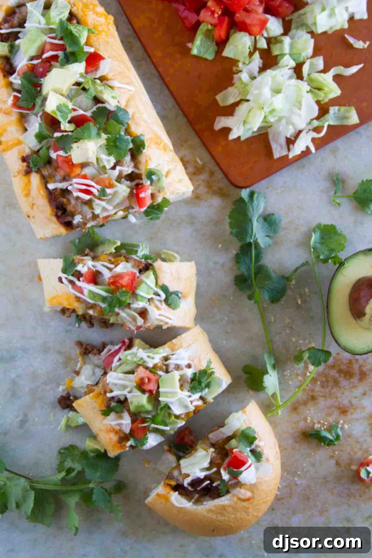 Crispy Taco Pizza Boats 6 A close-up of a fully assembled and sliced Taco French Bread Pizza, garnished with fresh lettuce, tomatoes, cilantro, and dollops of sour cream, ready to be enjoyed.