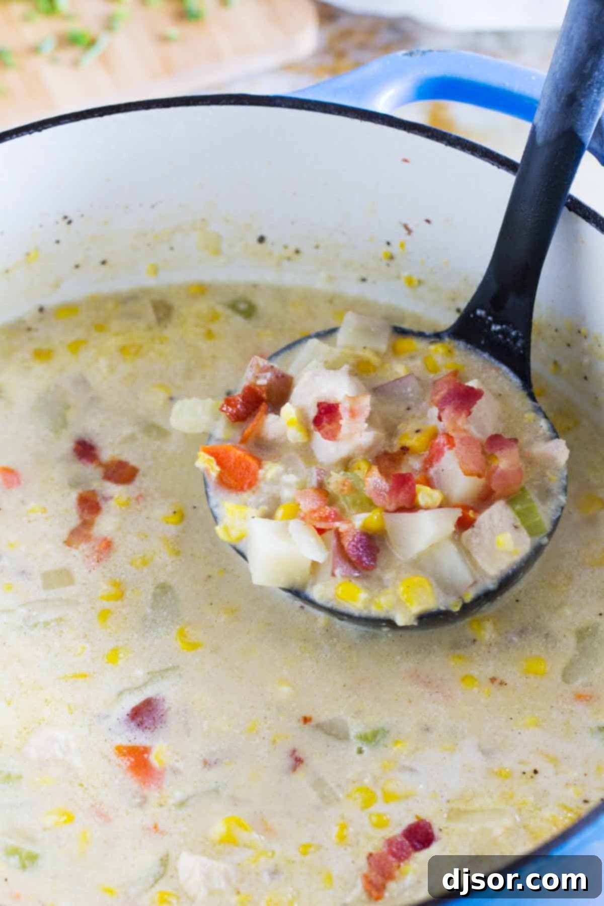 Ladle of Creamy Chicken Corn Chowder A ladle scooping a generous portion of thick, creamy chicken corn chowder from a rustic Dutch oven, showcasing chunks of chicken, potatoes, and corn.