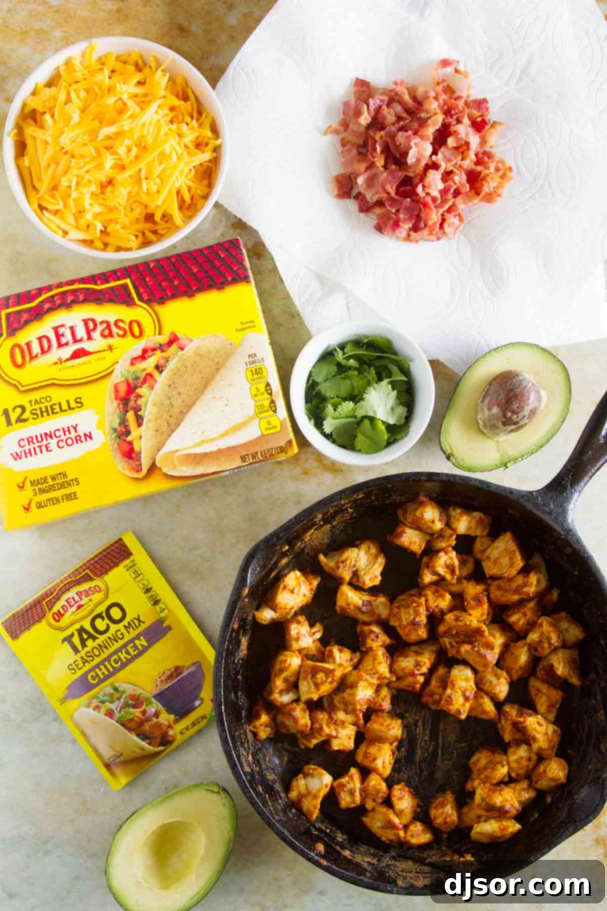 Stacked Chicken Bacon Avocado Tacos 3 Fresh ingredients laid out for Chicken Bacon Avocado Tacos, including raw chicken, strips of bacon, ripe avocados, taco shells, and Old El Paso seasoning.
