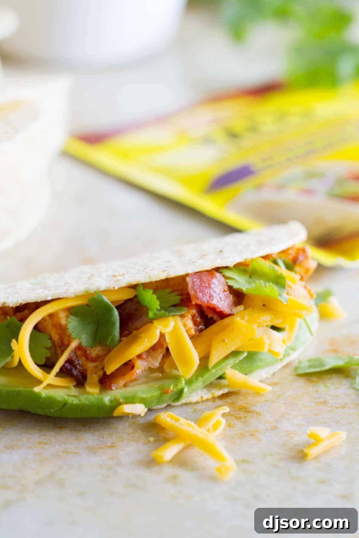 Stacked Chicken Bacon Avocado Tacos 5 A single Chicken Bacon Avocado Taco, perfectly assembled with generous amounts of shredded cheese, peeking out from a crunchy hard shell.