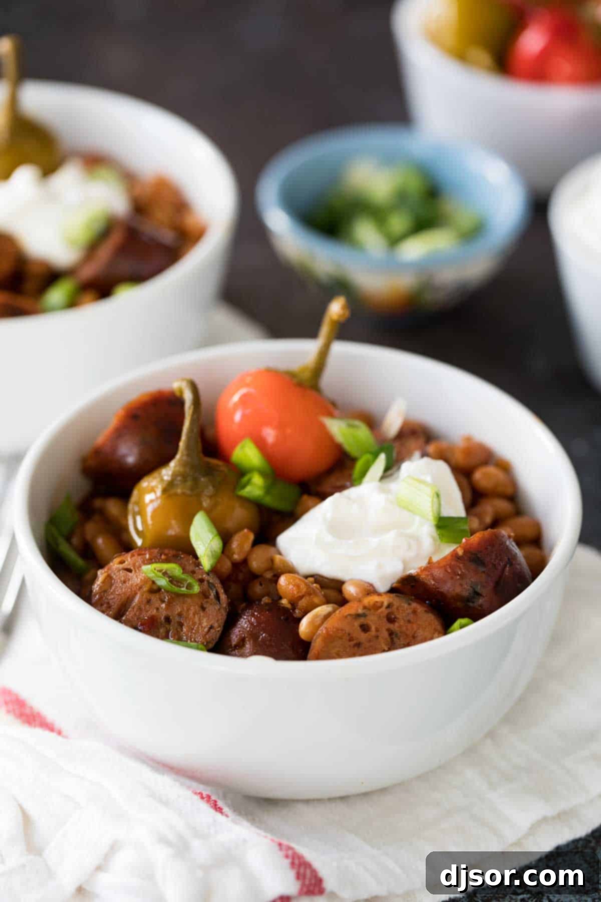 Slow Cooker Barbecue Beans and Sausage: A Hearty, Frugal Family Favorite White bowl filled with beans, sausage, sour cream, and peppers.