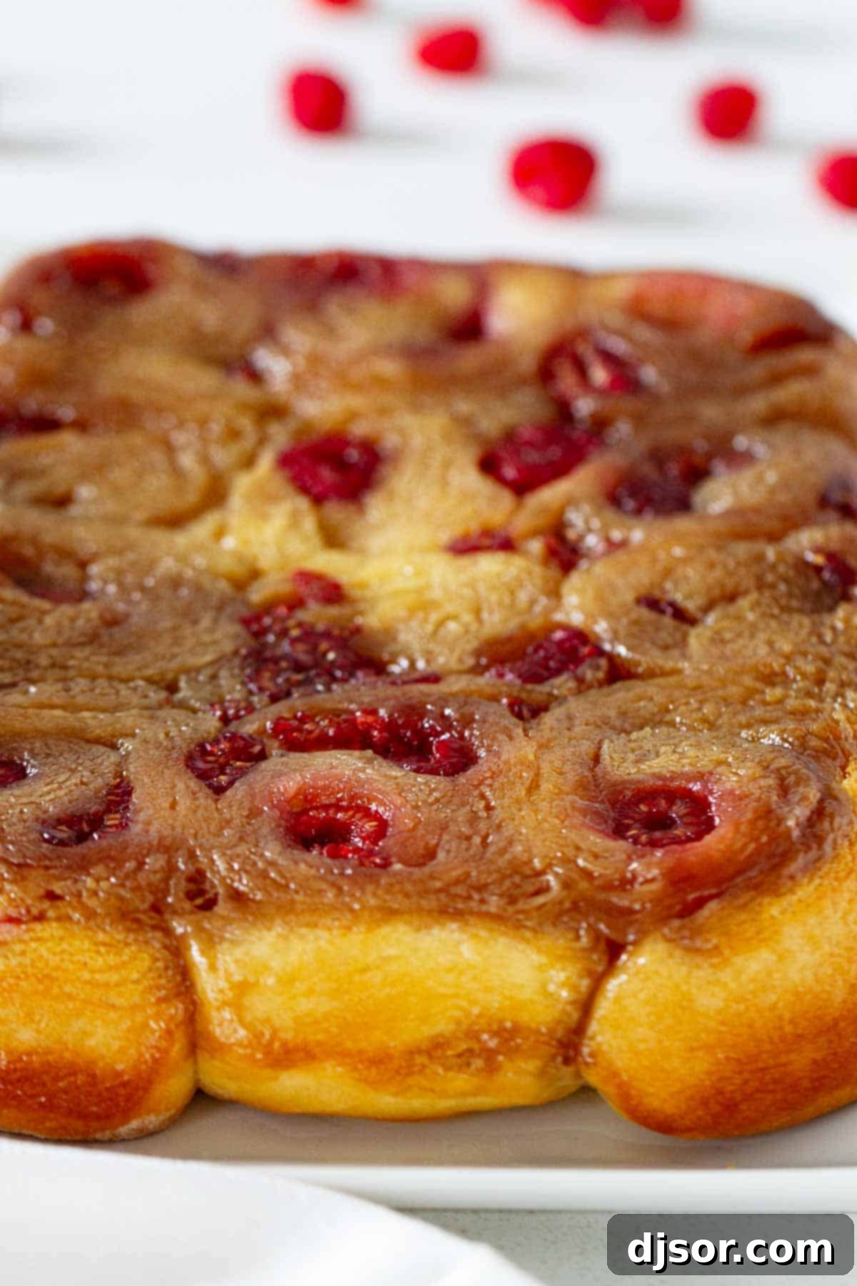A full pan of beautifully baked Raspberry Caramel Sticky Buns, glistening with caramel and dotted with raspberries, ready to be served.