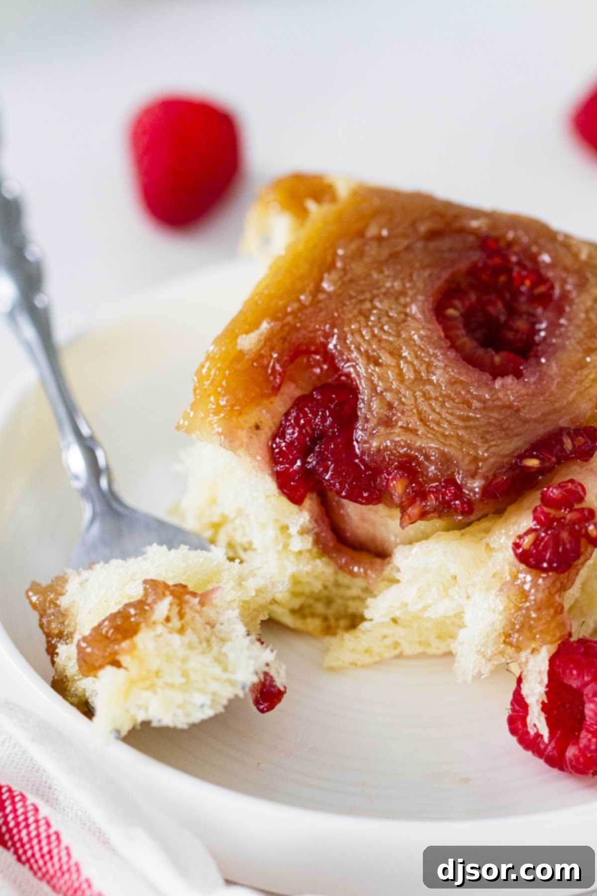 A single Raspberry Caramel Sticky Bun on a white plate, with a bite taken to reveal the soft, berry-filled interior and gooey caramel.