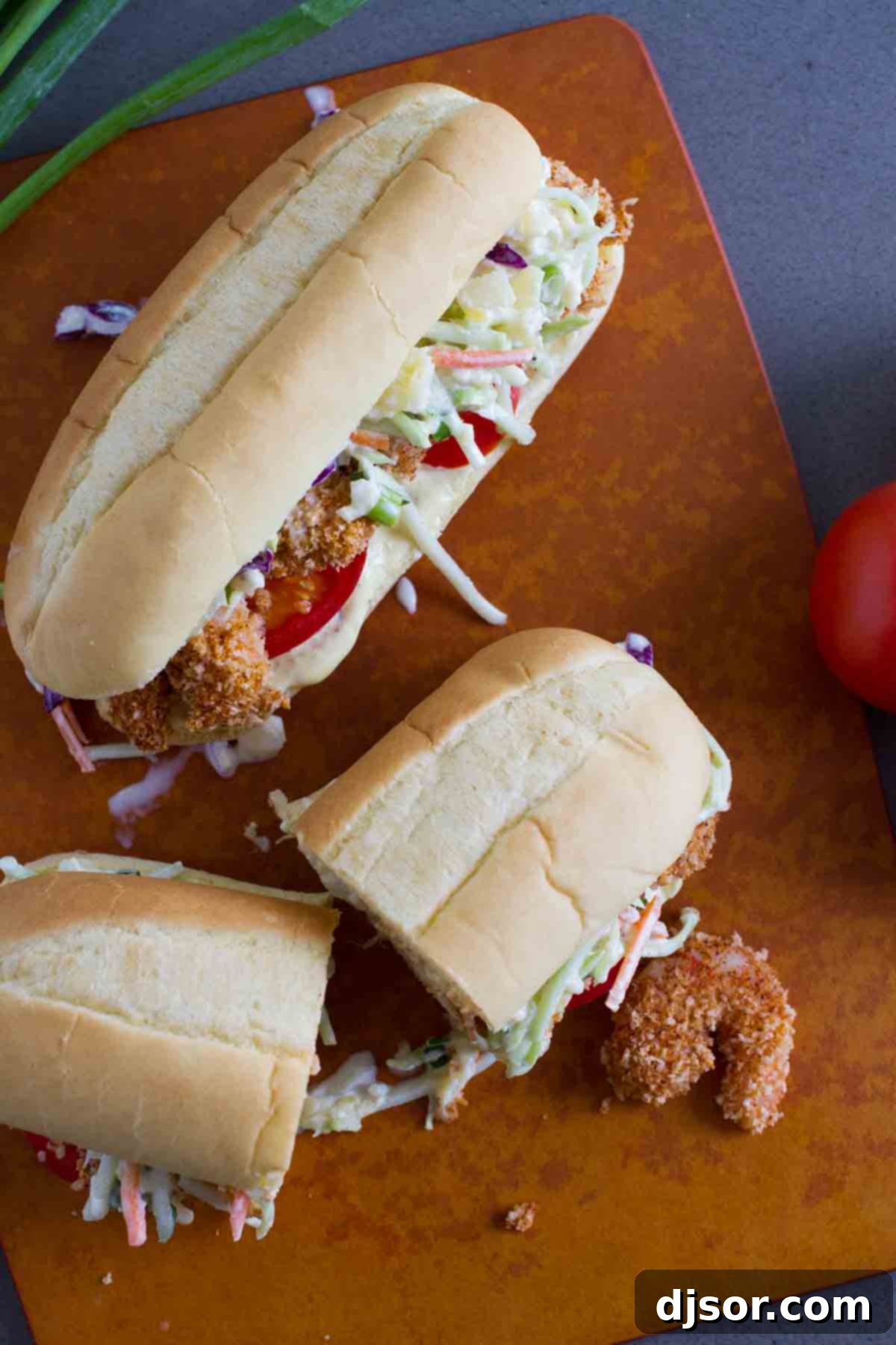 Two shrimp po boy sandwiches with one cut in half, showcasing the golden brown shrimp and colorful slaw.