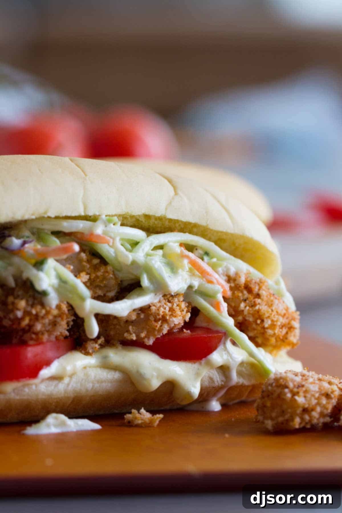Shrimp Po Boy sandwich with creamy sauce, tomatoes, baked shrimp, and pineapple slaw in a close-up view.