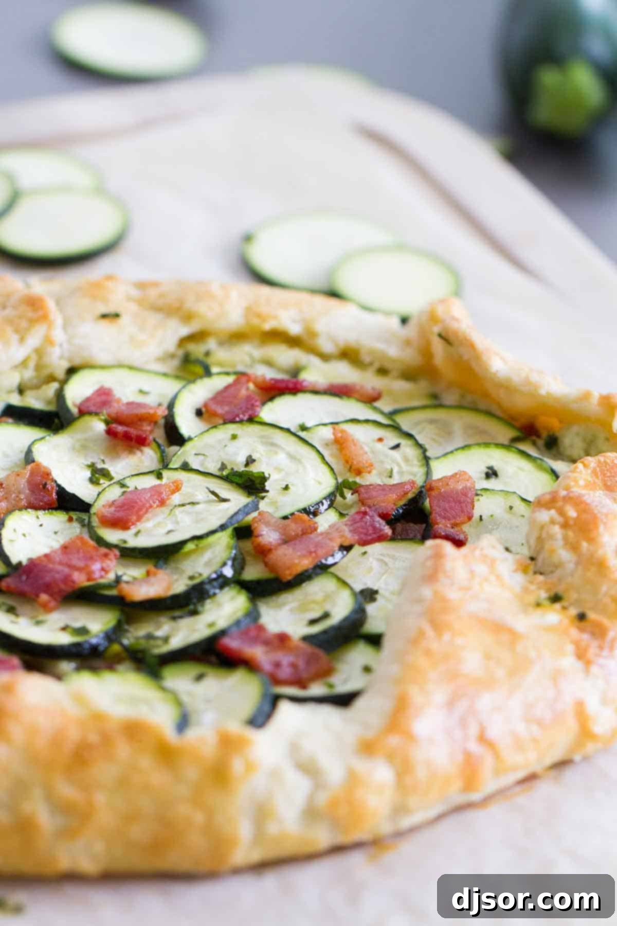 A tender, flaky crust is filled with a creamy ricotta filling, then topped with bacon and zucchini in this easy Zucchini Tart with Ricotta and Bacon that is perfect for a luncheon or a light dinner. Full zucchini tart with ricotta and bacon on a cutting board, ready to be sliced and served for a delicious meal.