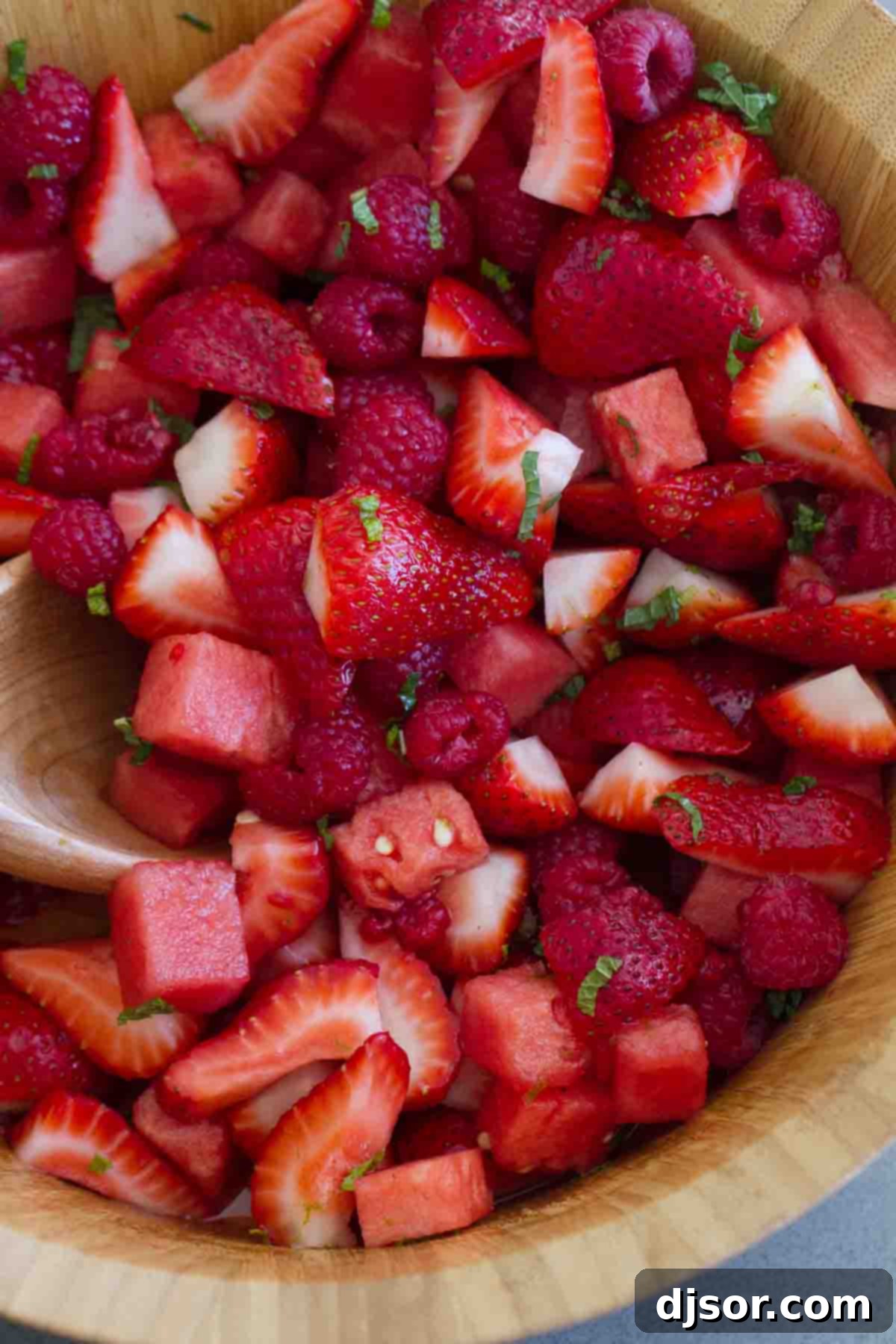 Crown Ruby Fruit Salad - Easy Watermelon, Strawberry, Raspberry with Lime Mint Dressing A vibrant bowl of Crown Ruby Fruit Salad featuring ripe watermelon cubes, halved strawberries, and whole raspberries, garnished with fresh mint leaves, and drizzled with a light lime dressing.