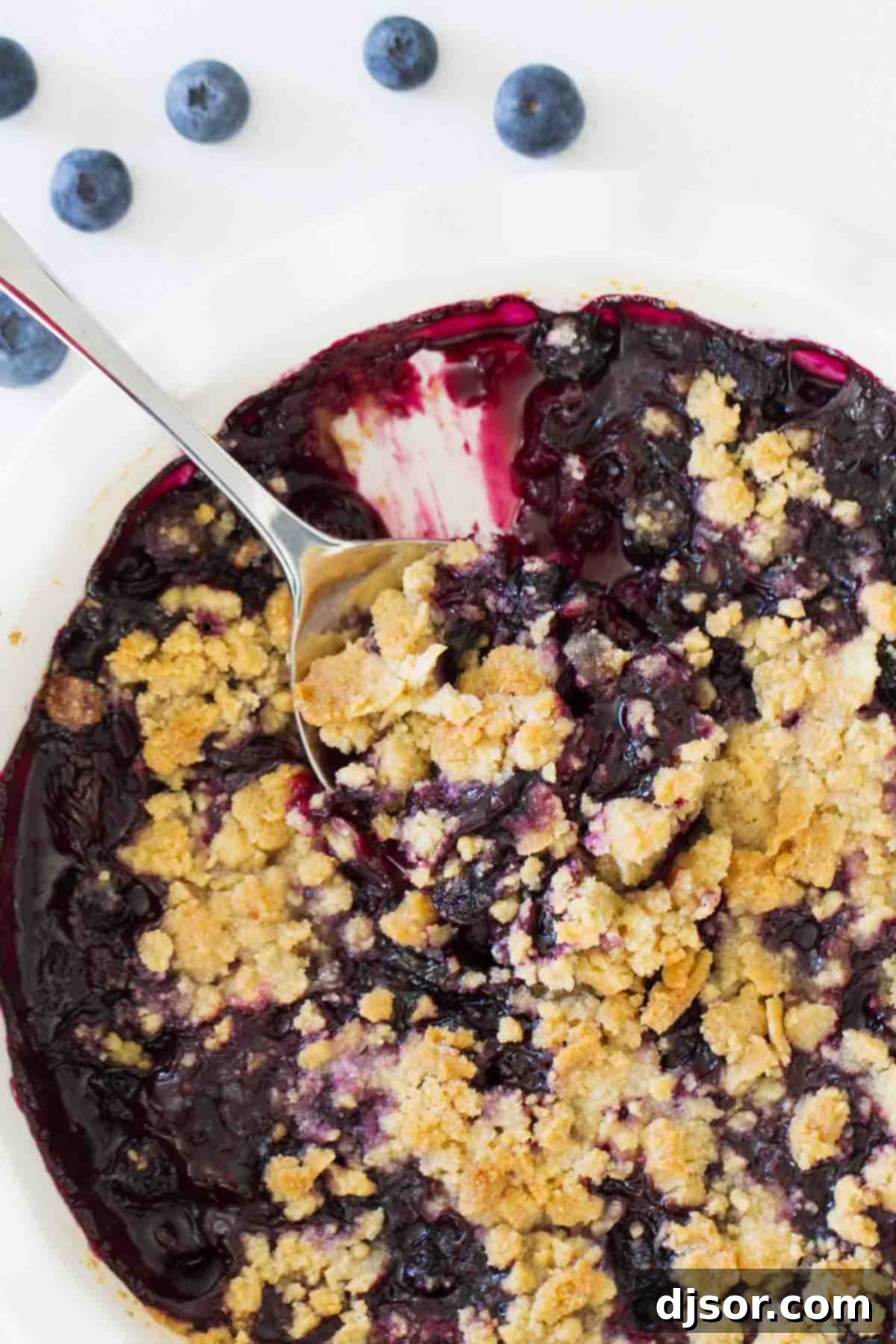 A serving dish of golden-brown blueberry crisp with a spoon, ready to be enjoyed.