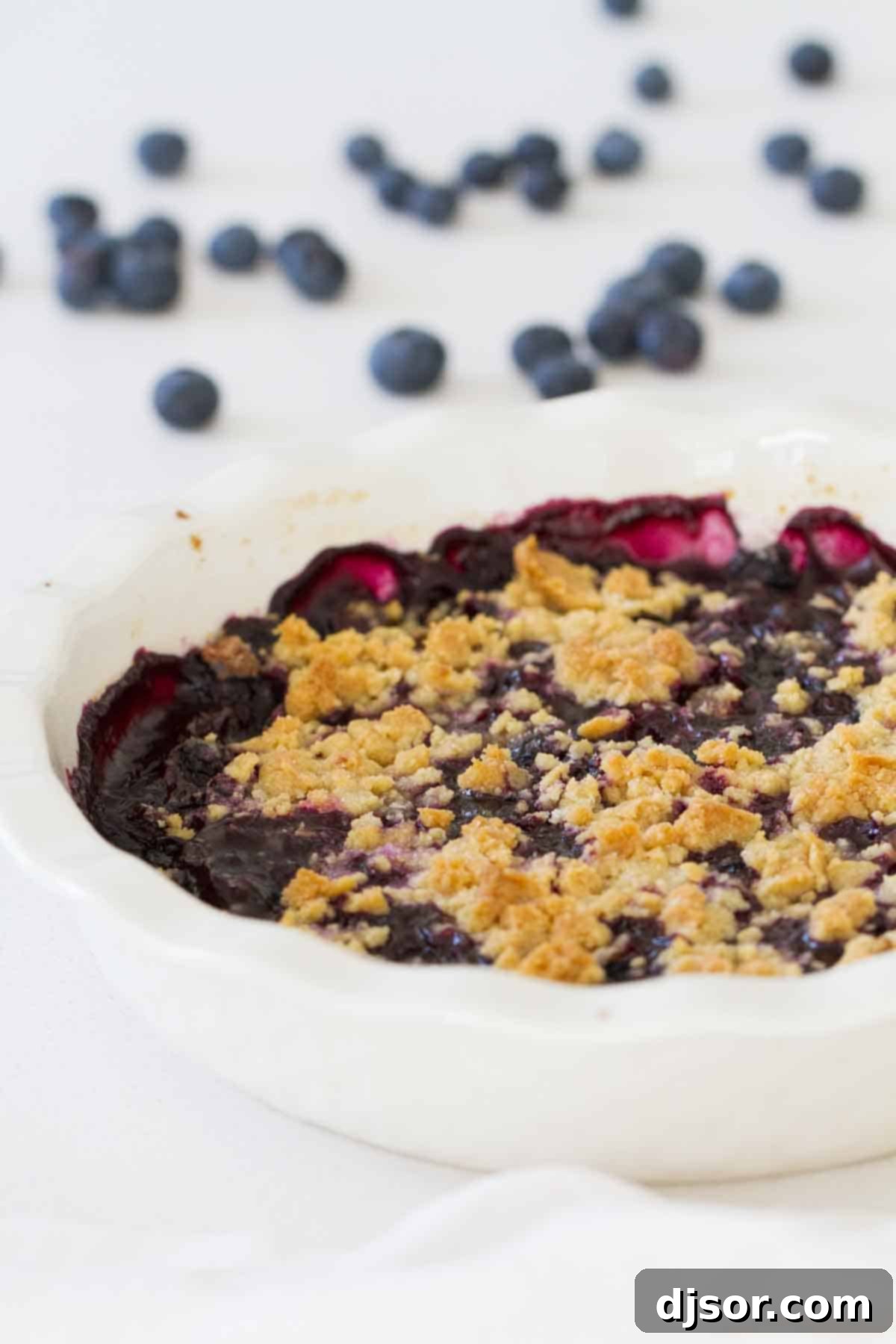 Close-up of a warm blueberry crisp with a crunchy golden topping, served in a round baking dish.