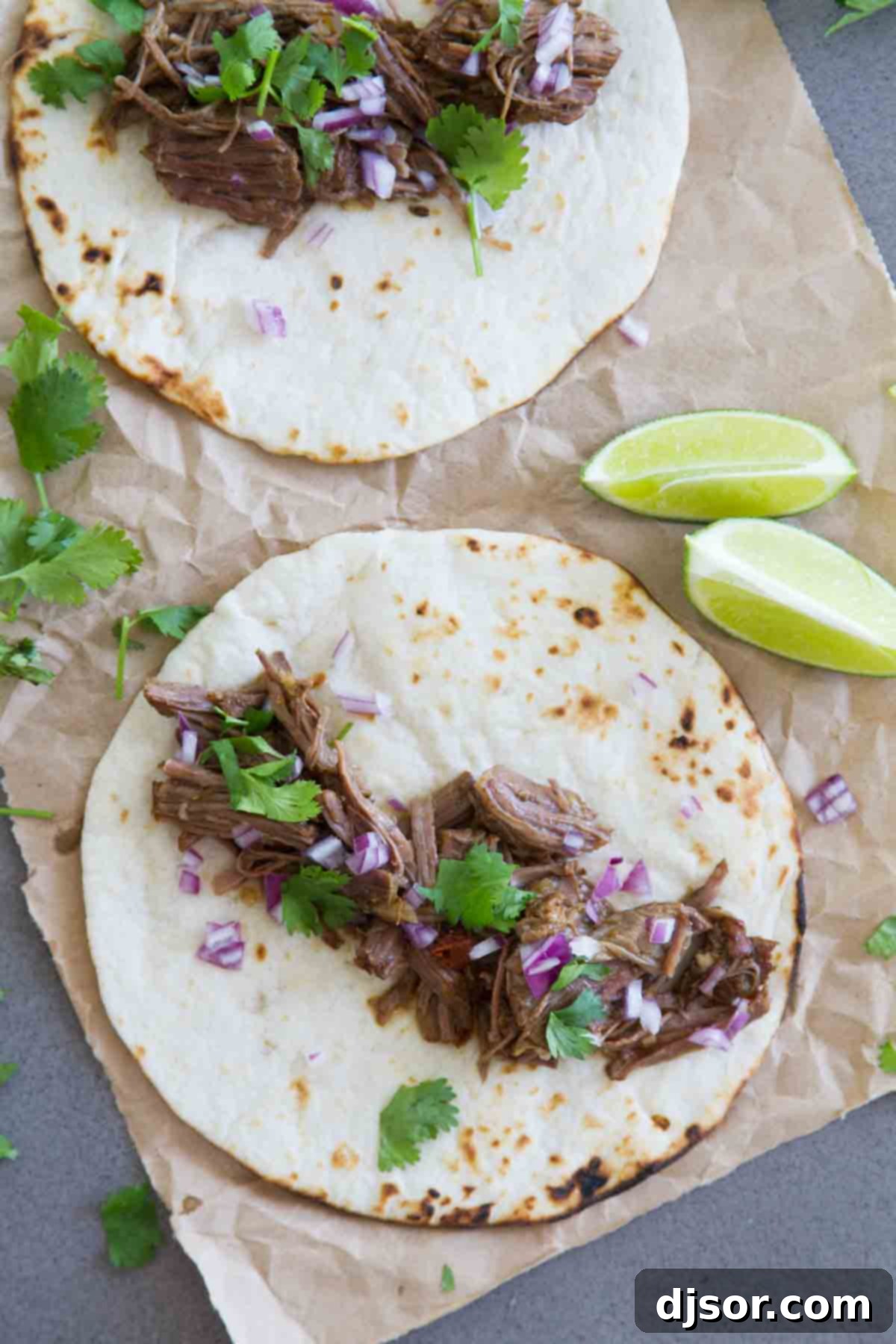 Spice up dinner in a fraction of the time with this Beef Barbacoa in the Instant Pot! Chipotle and cumin make this perfect for tacos, burritos, enchiladas and more! Overhead view of two delicious beef barbacoa tacos, topped with vibrant green cilantro and finely diced red onion.