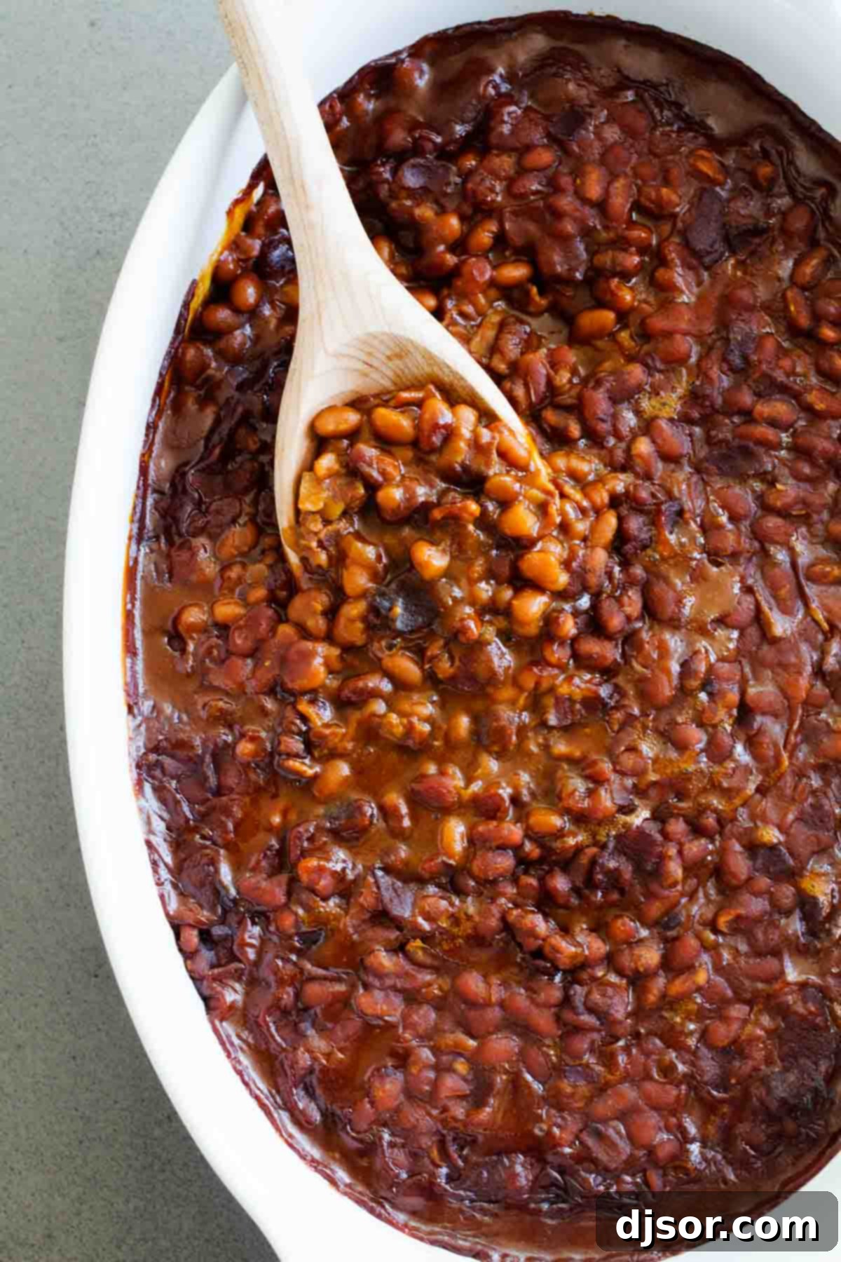 Overhead view of a generous dish of homemade baked beans with bacon, showcasing the glossy sauce and perfectly cooked ingredients.