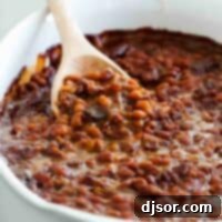 Baked beans with bacon in a casserole dish with a wooden spoon to scoop