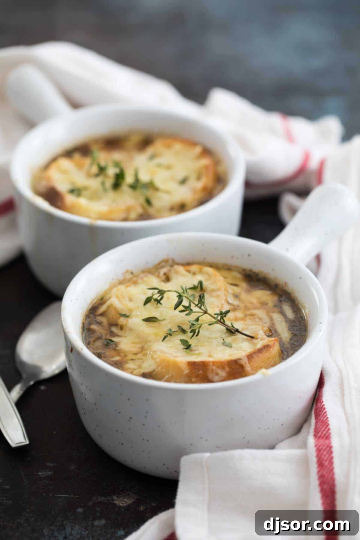Two steaming bowls of French onion soup, topped with golden-brown bread and melted Gruyere cheese, garnished with fresh thyme