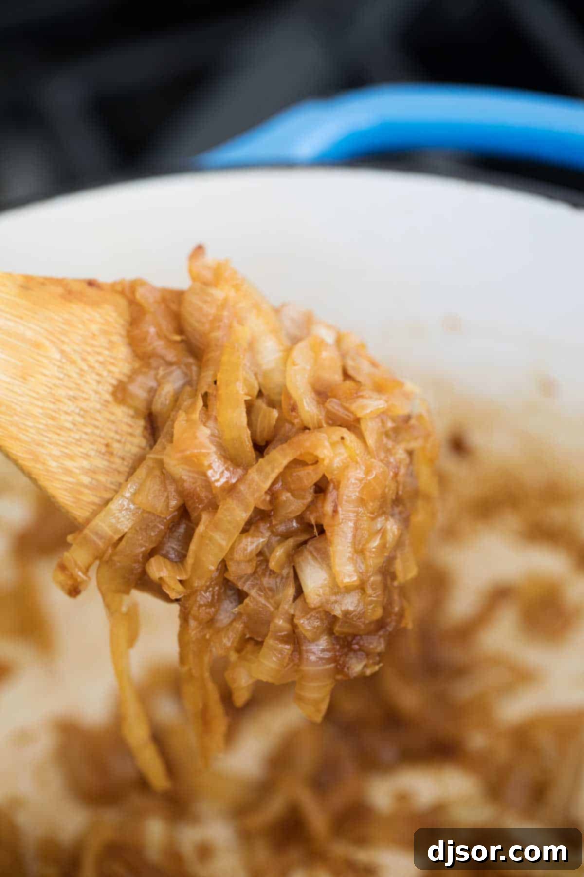 A wooden spoon scooping up perfectly caramelized onions, showcasing their deep brown color and soft texture