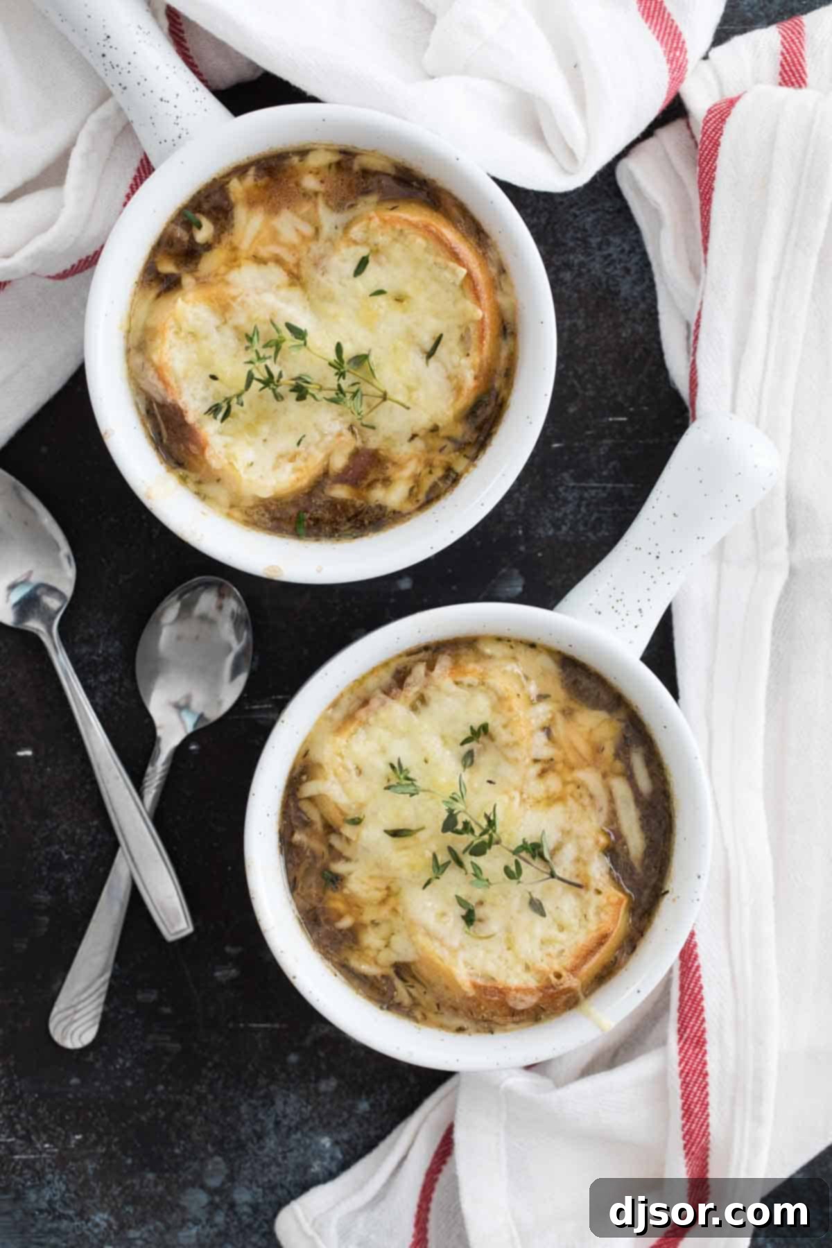 Overhead view of four oven-safe bowls filled with French onion soup, topped with baguette slices and a generous layer of shredded cheese, ready for the oven