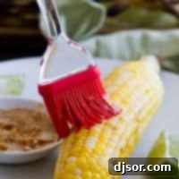 Flame-Kissed Corn with Savory Smoked Butter 2 brushing butter on a cob of grilled corn