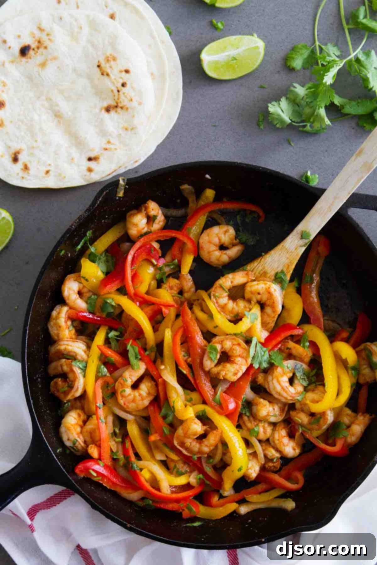 Shrimp Fajitas in a Cast Iron Skillet with warm tortillas and fresh lime wedges on the side, ready to be served.
