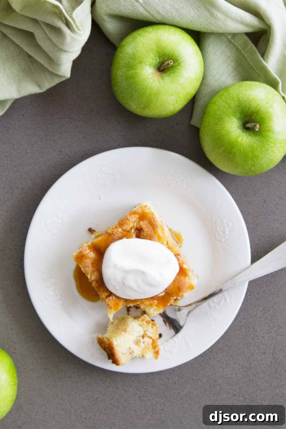 An overhead shot showcasing a full Apple Cinnamon Cake, with several fresh apples artfully arranged around it on a rustic wooden table, highlighting the natural ingredients.