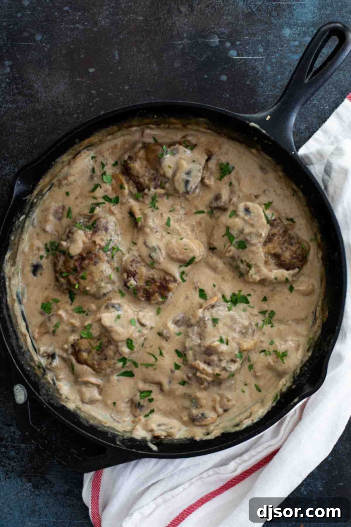 An inexpensive, filling and comforting meal that is family friendly and full of flavor, this Salisbury Steak Recipe is a childhood throwback that you’ll want to make over and over again. Salisbury steak with rich brown gravy in a cast iron pan, ready to be served.