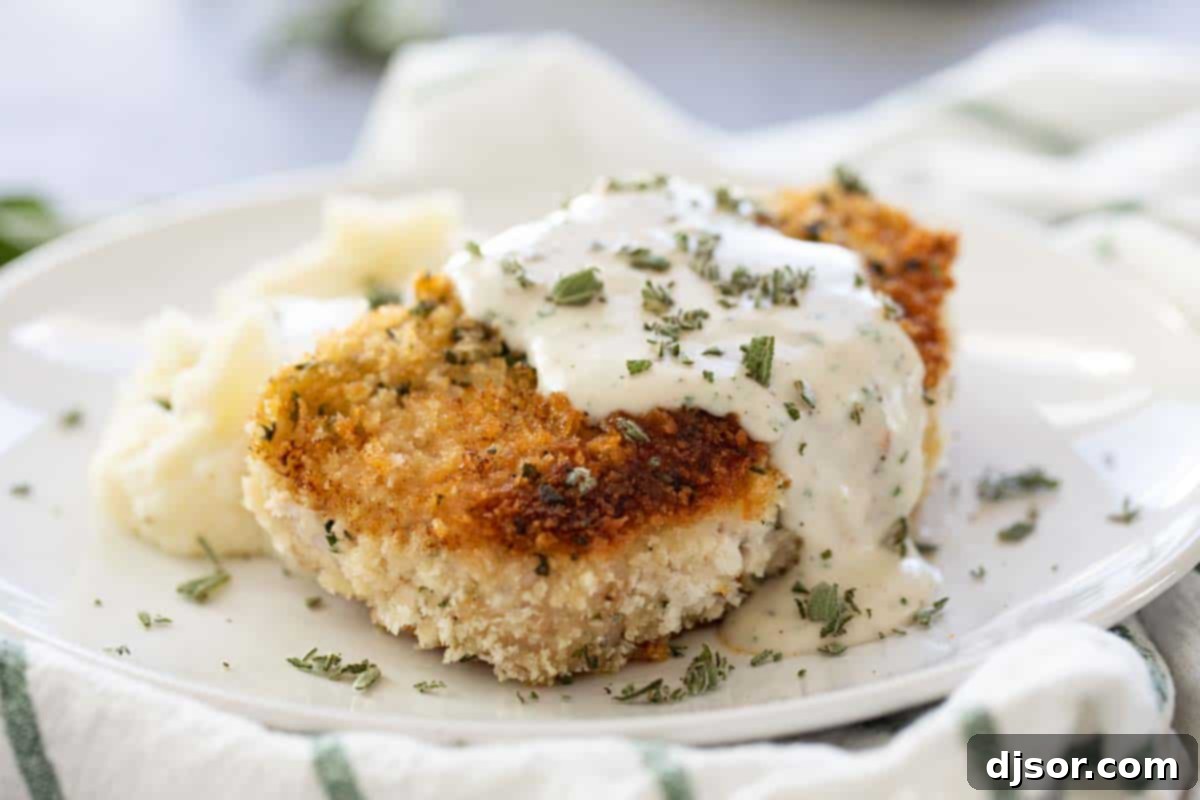 Crispy breaded pork chop with cream gravy on a plate, ready to be served.