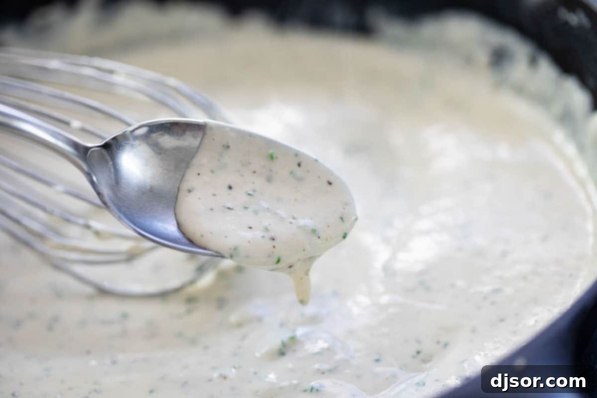 Close-up of creamy gravy infused with fresh parsley and sage, simmering in a skillet.