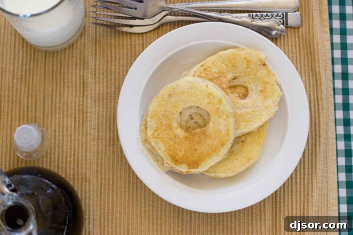 Apple Pancake Rings - Fresh apples sliced and dipped in pancake batter, then cooked until golden. Great for breakfast or for an after school snack! Overhead view of several golden-brown Apple Pancake Rings dusted with powdered sugar, arranged on a rustic wooden board, ready to be served for breakfast or a snack.