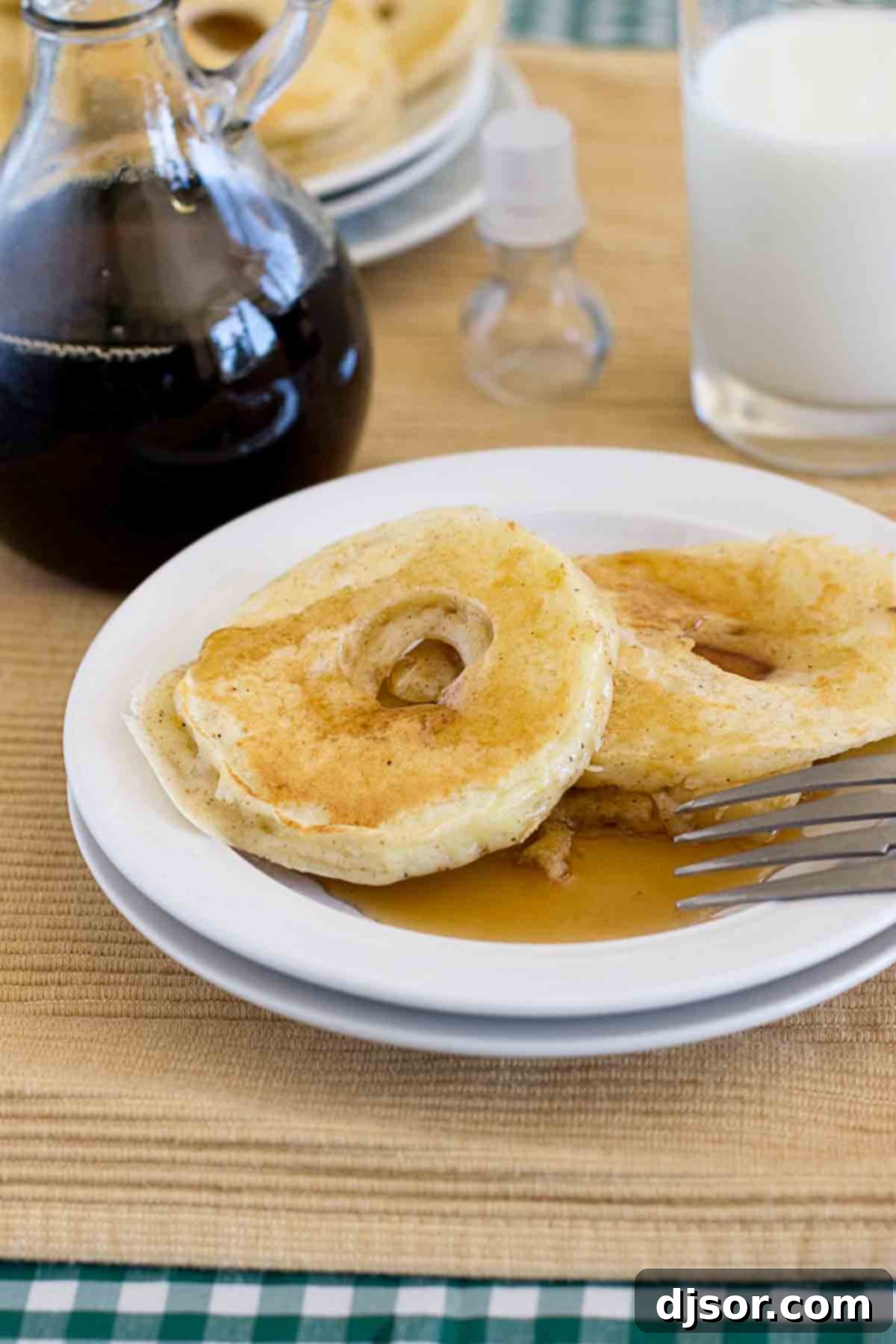 Apple Pancake Rings - Fresh apples sliced and dipped in pancake batter, then cooked until golden. Great for breakfast or for an after school snack! A stack of golden-brown Apple Pancake Rings served on a white plate, drizzled generously with maple syrup and garnished with fresh apple slices, ready to be enjoyed.