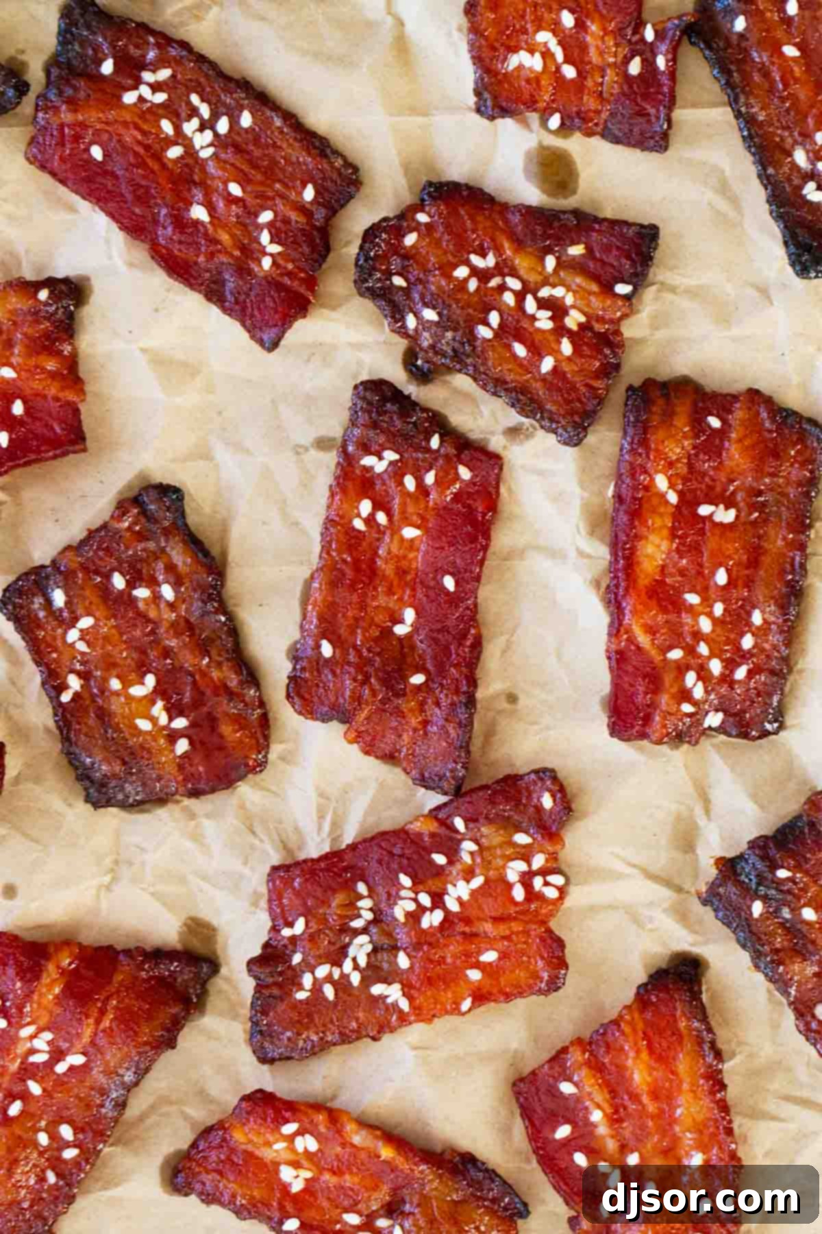 A plate of crispy, glossy Brown Sugar Sriracha Bacon Bites sprinkled with sesame seeds. Brown Sugar Sriracha Bacon Bites topped with sesame seeds on a piece of parchment paper, ready to be served.