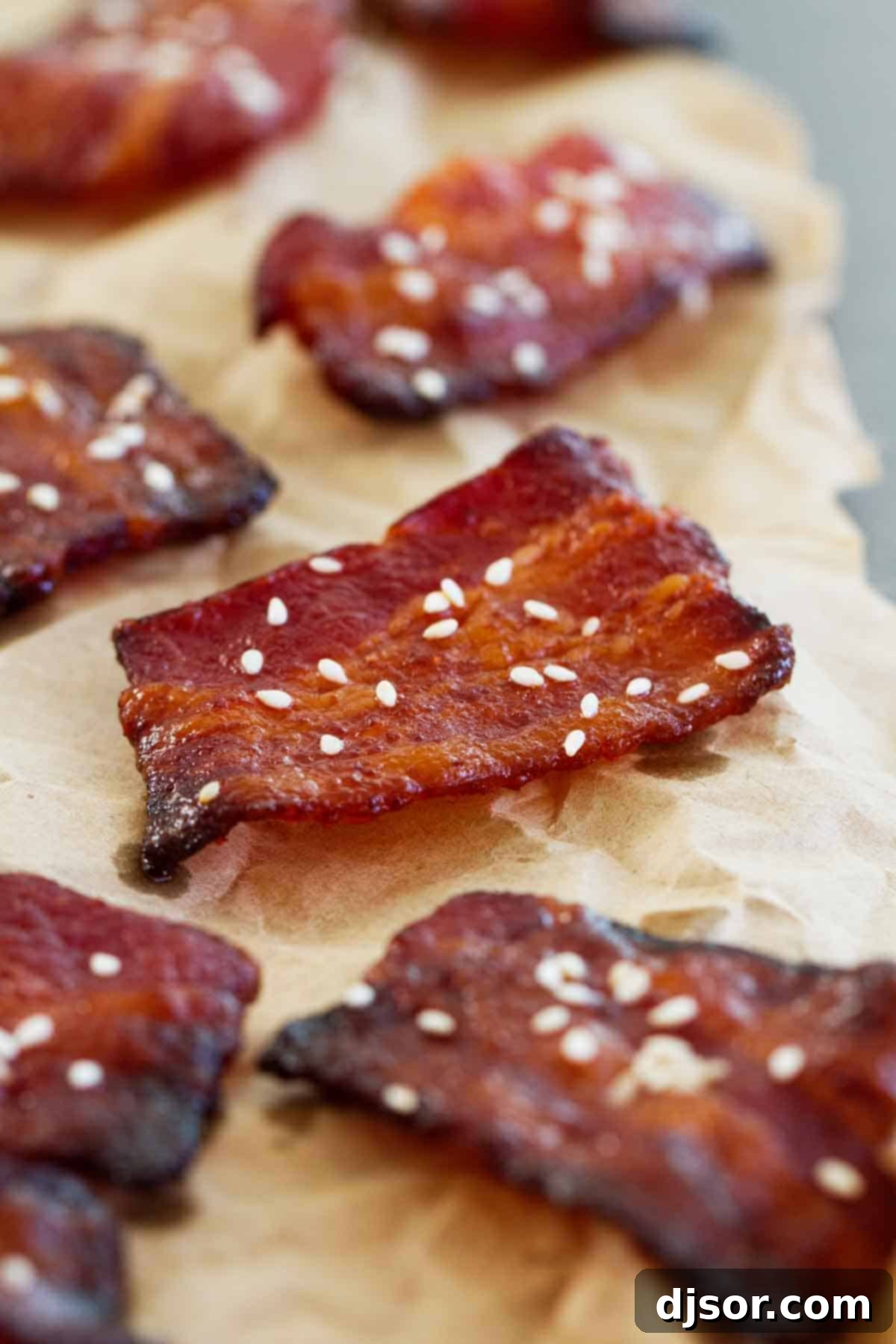 A platter of Brown Sugar Sriracha Bacon Bites, glistening with their sweet and spicy glaze. Close-up of Brown Sugar Sriracha Bacon Bites topped with sesame seeds, showing their glazed texture.