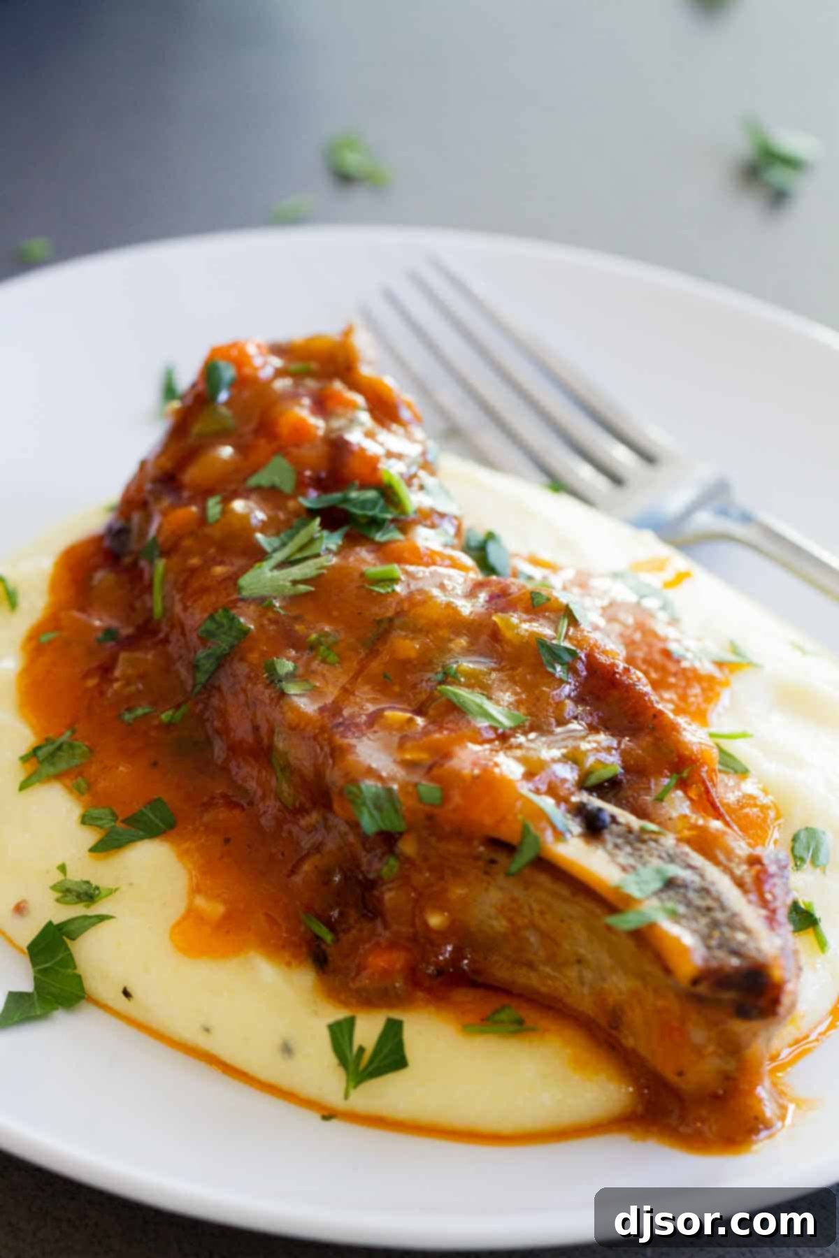 Close-up of Braised Country Style Pork Ribs served over creamy polenta, garnished with fresh herbs.