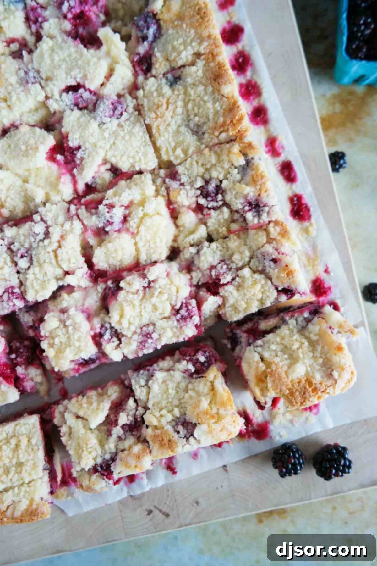 A pan full of freshly baked Blackberry Pie Bars, neatly cut into squares, showcasing the layered texture of crust, filling, and streusel.