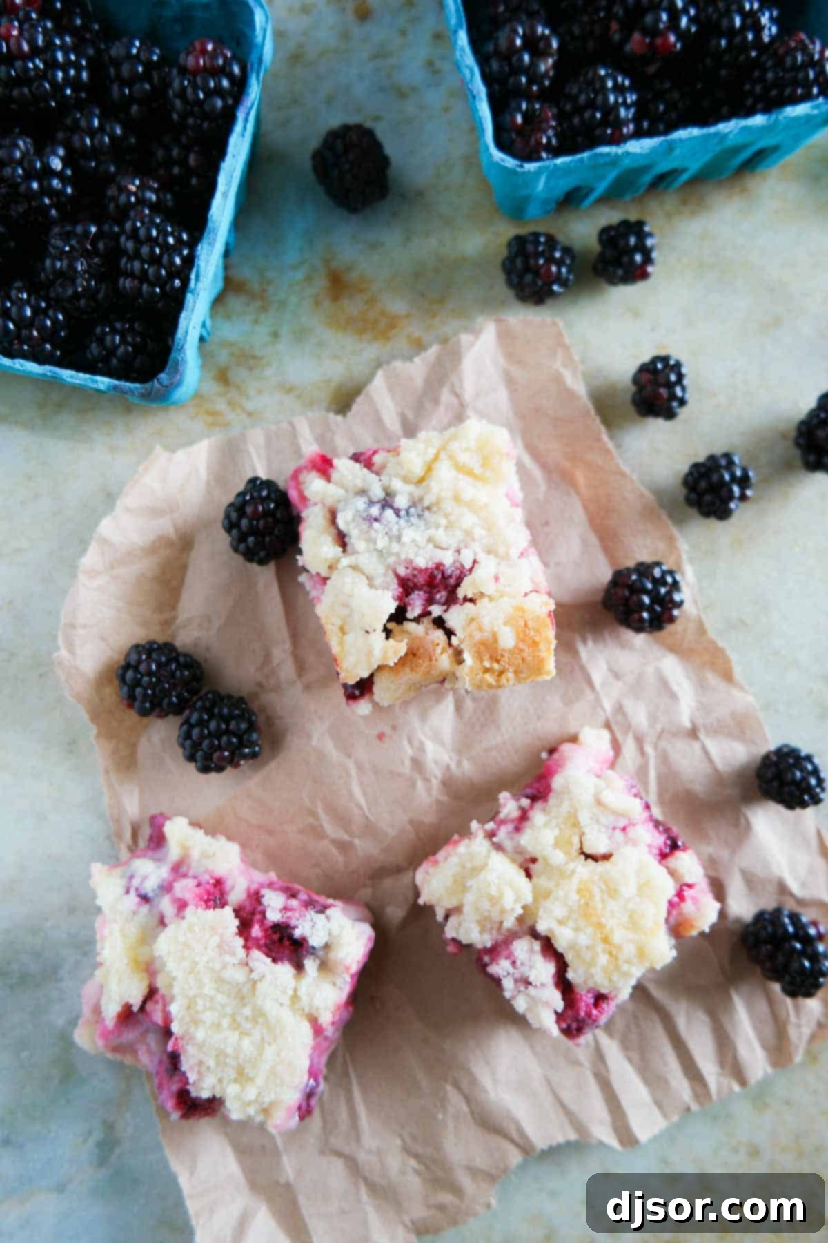 Blackberry pie bars cut into squares are displayed on a white plate, with fresh blackberries scattered alongside.