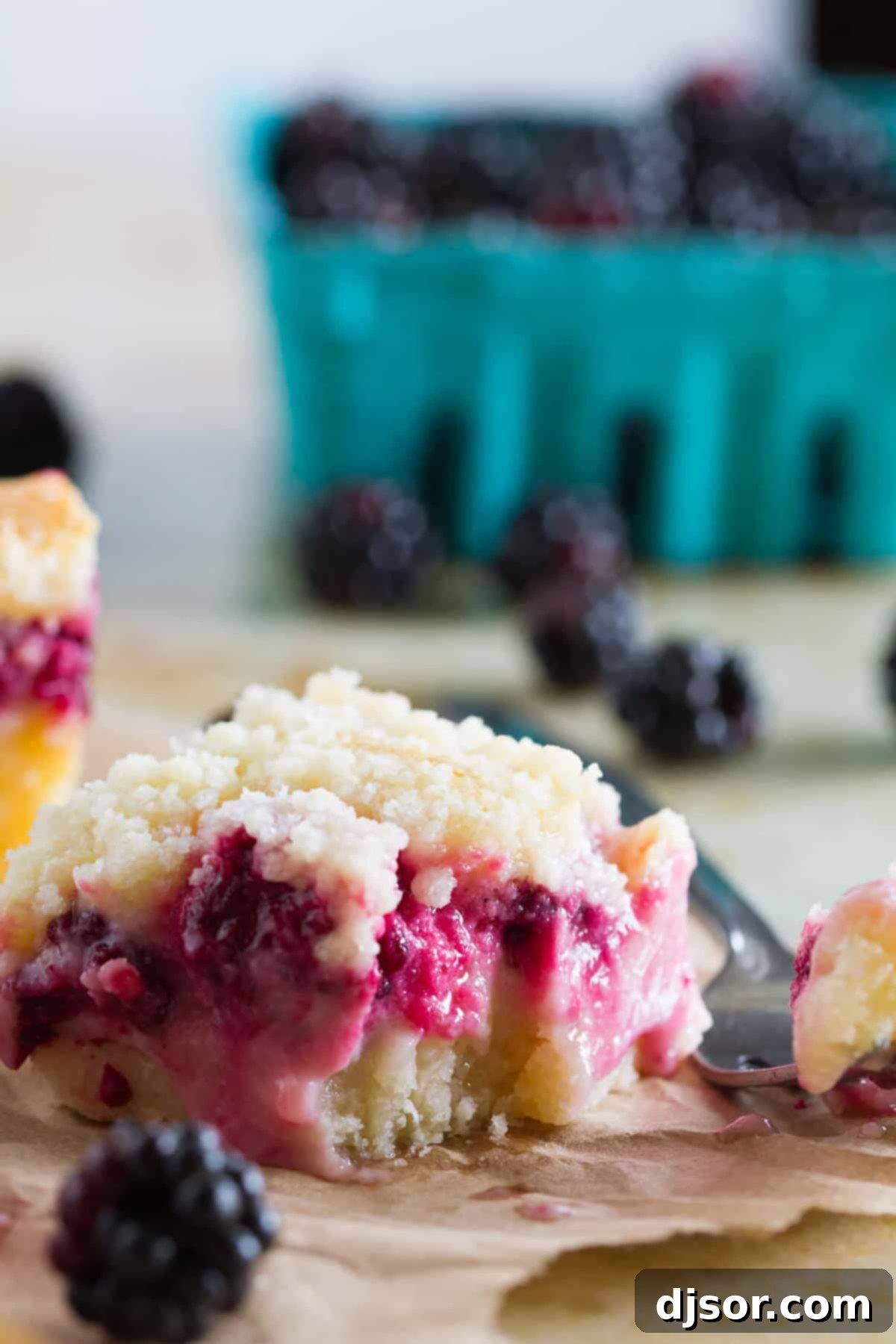 A close-up of a Blackberry Pie Bar with a bite taken out, revealing the layers of crust, creamy filling, and streusel topping.